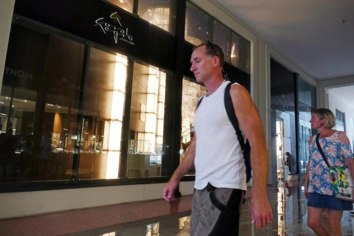 Tourists, trying to keep dry during a passing downpour of rain, walk by Coral Negro, a new jewelry store on the first level of the Gran Hotel Manzana Kempinski in Old Havana.