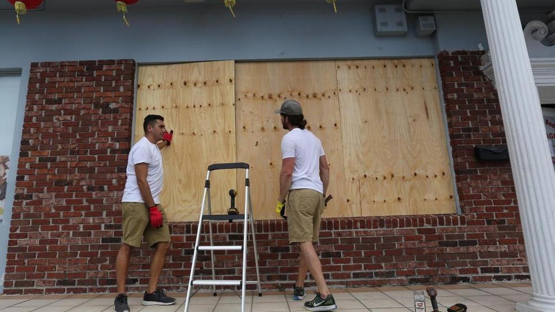 Two men protect a LeJeune Road shopping center with plywood Wednesday.