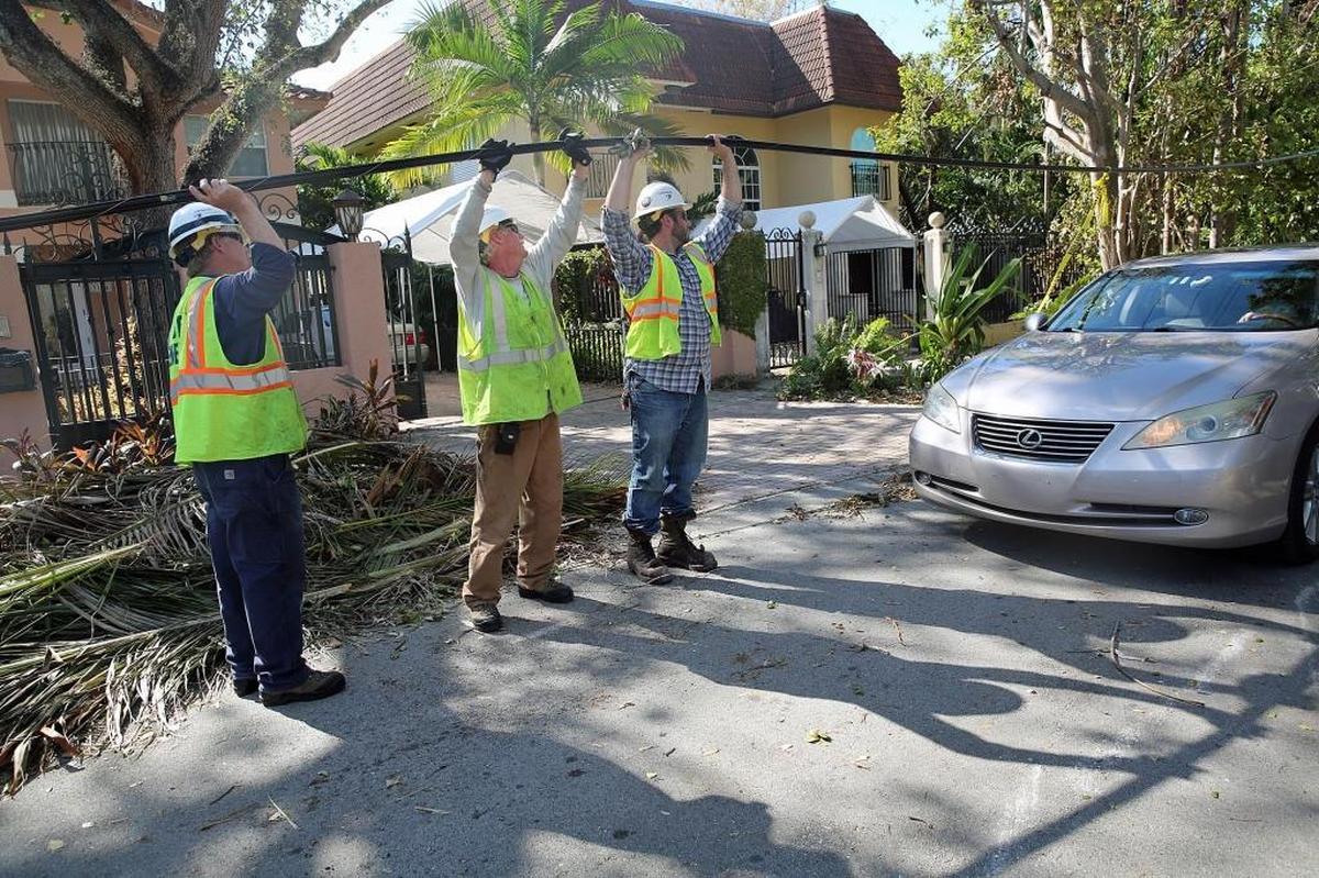A crew from DTE Energy of Michigan — Duke Carlos, left, Rich Buko, middle, and Mark Salvatori — lift a telecommunications cable so a Miami resident can park in her driveway. They also restored power Friday to hundreds of homes.
