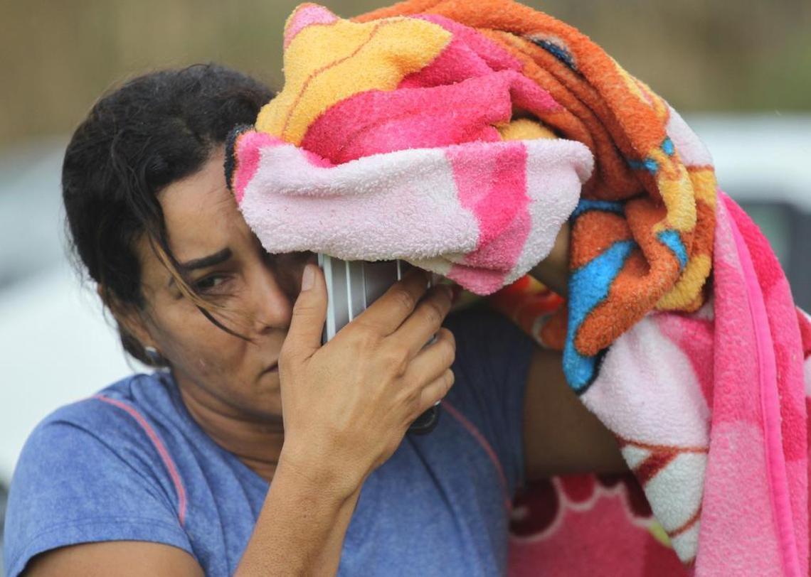 A woman uses a towel to shield herself from the rain as she attempts to call the U.S. mainland. About forty vehicles pulled to the shoulder as locals tried to place calls to the U.S. mainland near a cell tower outside of Dorado on PR22 in Puerto Rico on Saturday.