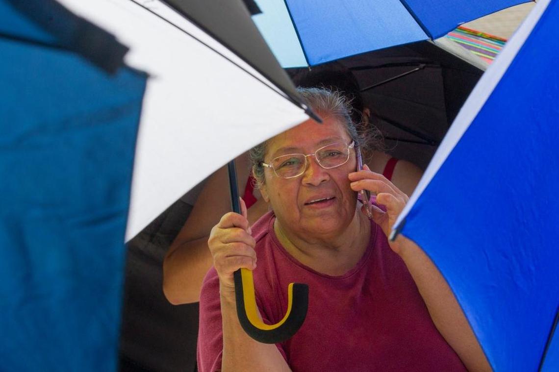 Teodora Garcia, 64, talks on the phone while holding her umbrella and waiting in line to receive food and water Friday from Farm Share and Miami-Dade Public Schools at the Homestead Housing Authority.