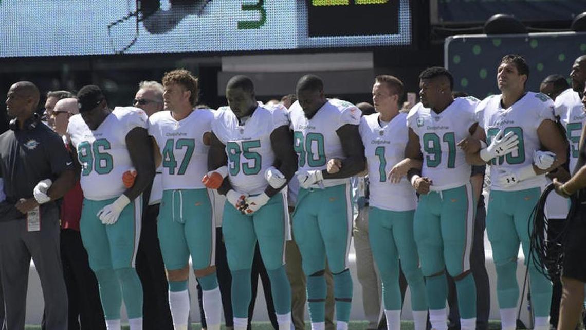 Miami Dolphins players lock arms during the playing of the national anthem before an NFL football game against the Jets Sunday.