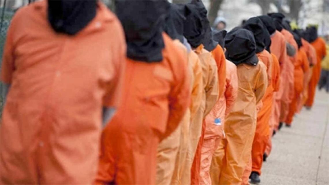 Detainees, in orange suits and hoods, line up at Guantánamo detention center.
