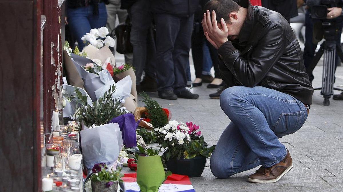 A man holds his head in his hands as he lays flowers in front of the Carillon cafe, in Paris, Saturday, Nov.14, 2015. French President Francois Hollande vowed to attack Islamic State without mercy as the jihadist group admitted responsibility Saturday for orchestrating the deadliest attacks inflicted on France since World War II.