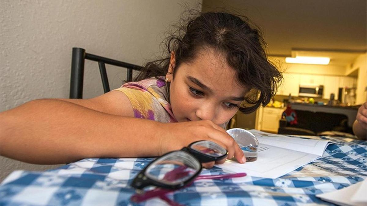 Yasmine Shabaneh of Tallahassee reads with the help of a magnifying glass. She and her brother were eliminated from a program for sick and disabled children, but then reinstated.