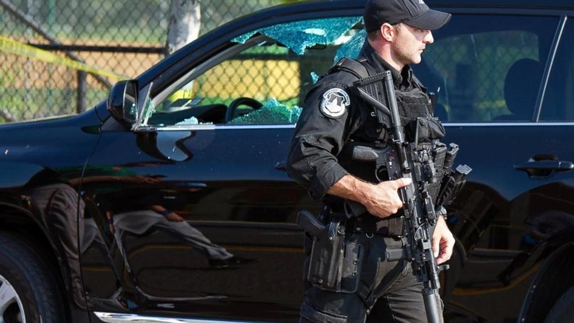 A Capitol Police officer walks past a car with a shattered window at the shooting site of a Congressional baseball practice.
