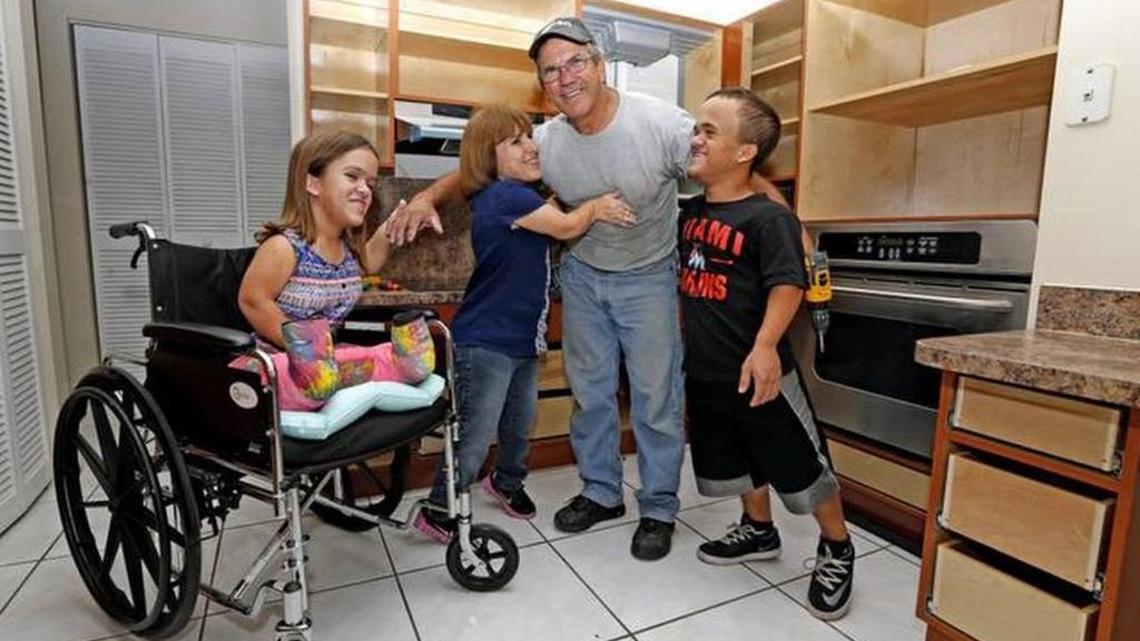 Carpenter Carlos Diaz gets a hug from Lissette Ference and her children Zach, and Alannah after the family’s The Ference family’s kitchen cabinets were lowered with help from Wish Book readers.