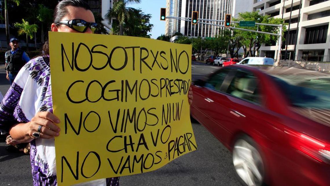 A protester in Puerto Rico holds a sign that reads: “We didn’t take out a loan. We didn’t see a dime. We’re not going to pay.”