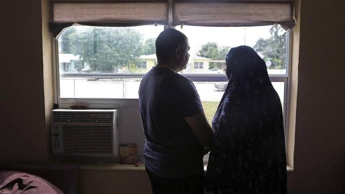 In Miami, Syrian refugees Mohamad, left, and Foza stand at the front window of their rented home.
