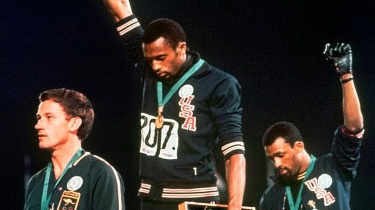 El medallista de oro olímpico estadounidense en 200 metros Tommie Smith, centro, y su compañero de equipo John Carlos, quien ganó el bronce, levantan los puños en protesta durante la reproducción del himno nacional de Estados Unidos en los Juegos de Verano de 1968 en la Ciudad de México. El medallista de plata australiano Peter Norman está a la izquierda.