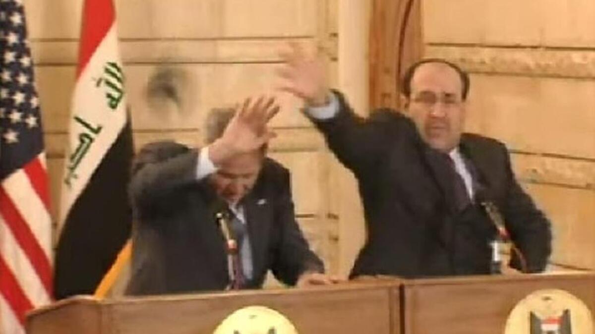 President George W. Bush, with Iraq Prime Minister Nouri al-Maliki, reach out to block a flying loafer.