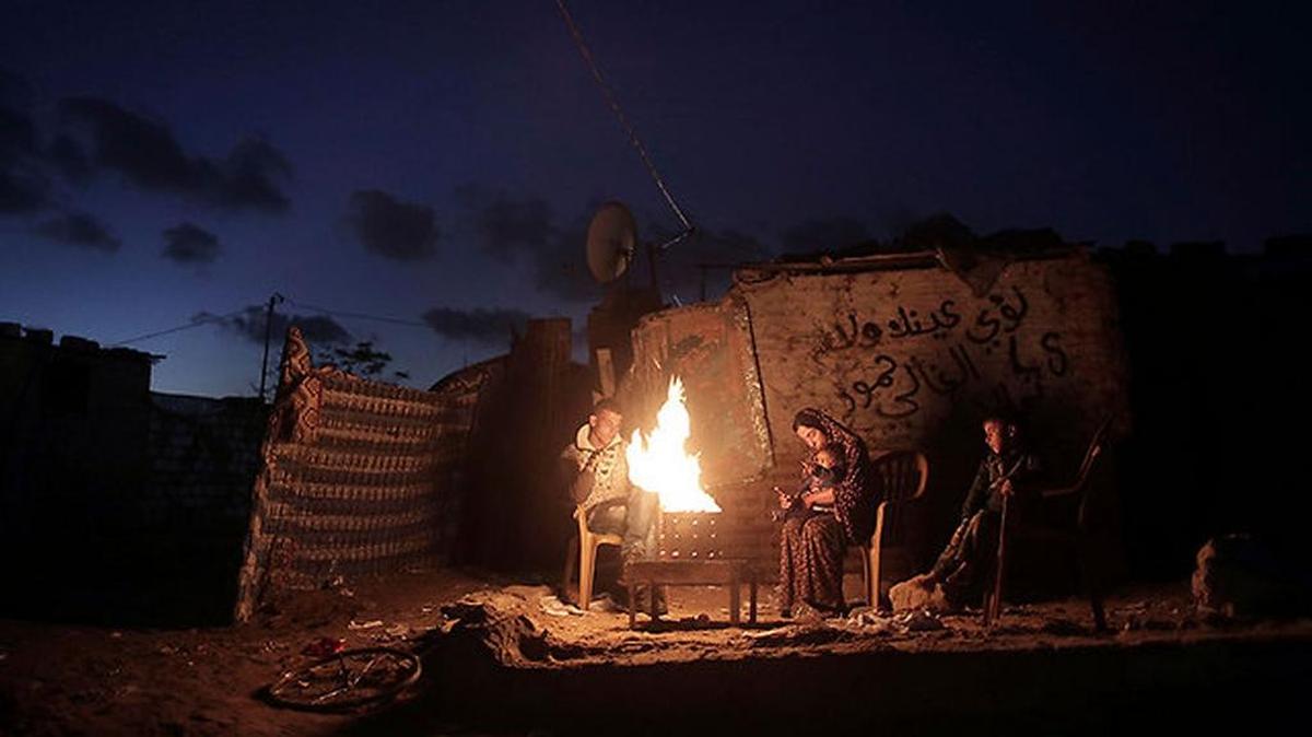 Gazan family in the city of Khan Unis live by the light of a fire during daily power outages.