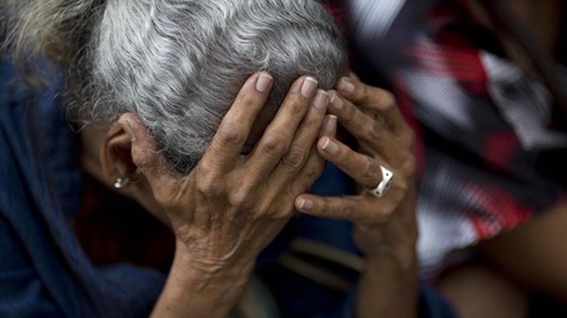 A woman holds her head as she waits in line outside a supermarket to buy scarce food in Caracas.
