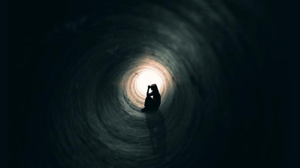 A woman prays as she sits in a dark tunnel.