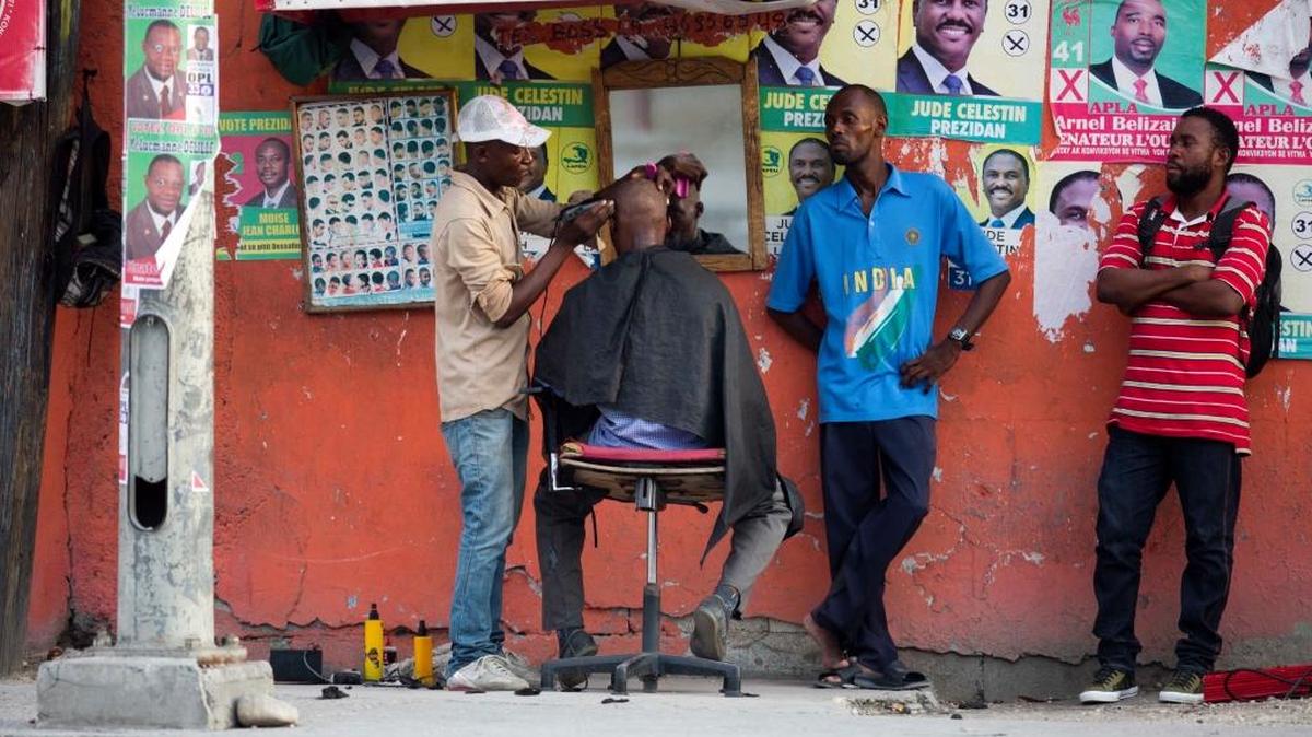 A street barber shop attends to customers next to a wall decorated with candidate posters in Port-au-Prince, days before the Oct. 9 vote.