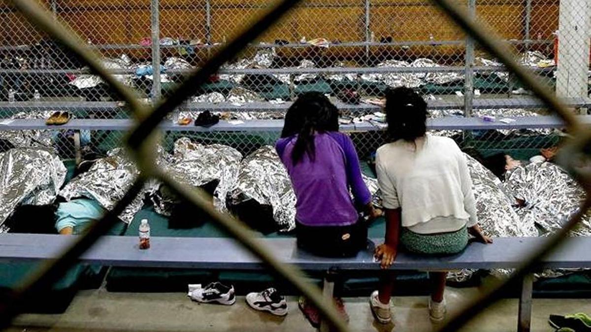 Two young girls watch television from their holding area where hundreds of mostly Central American immigrant children are being processed and held at the U.S. Customs and Border Protection Nogales Placement Center. The Central America summit in Miami hopes to find ways to let people remain in that native countries.