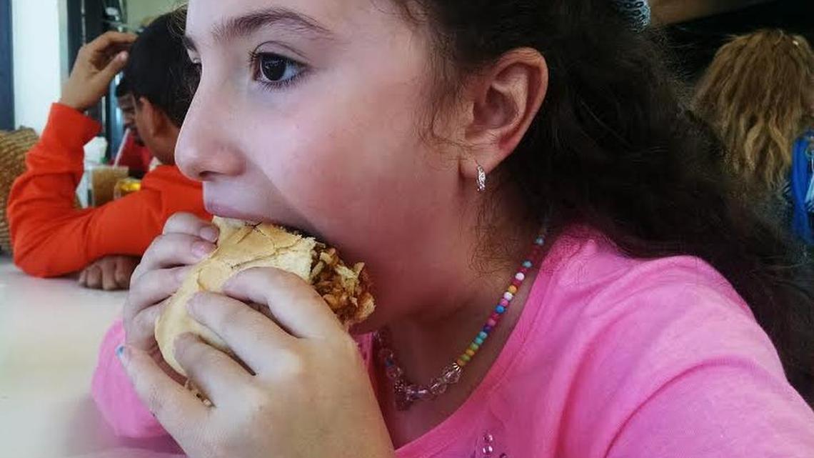 Young girl bites into a frita, a Miami staple since the 1960s.