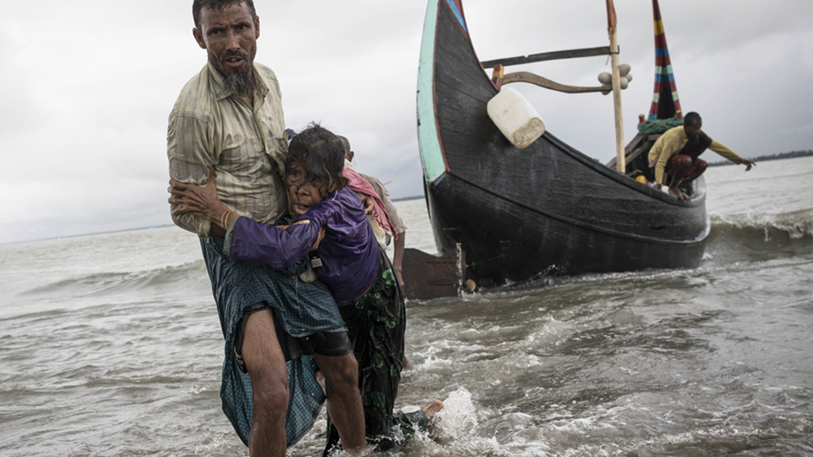 In September, a Rohingya man helps an elderly woman after their wooden boat, fleeing Myanmar crashed into the shore in Dakhinpara, Bangladesh.