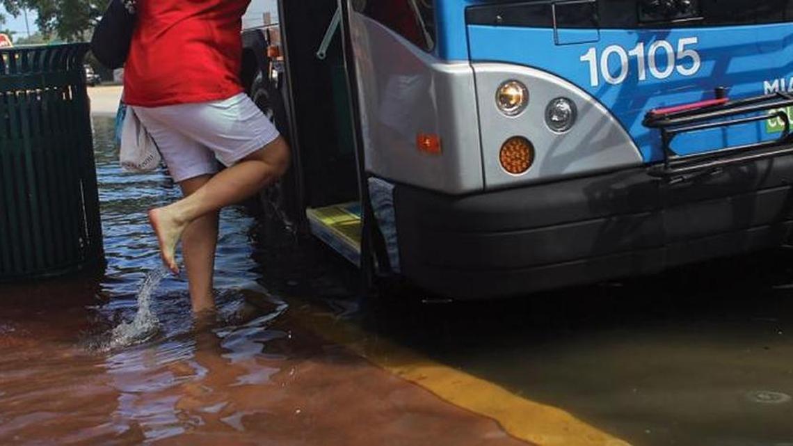 A woman enters a Miami-Dade County bus, boarding in her bare feet because of street flooding.