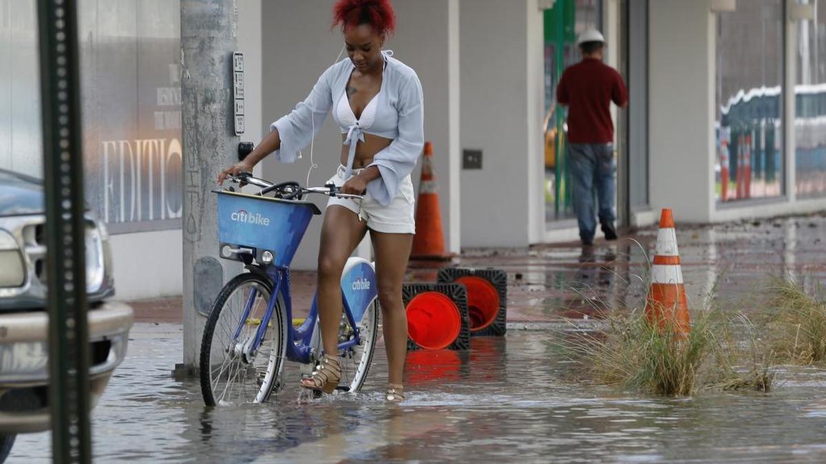 A woman walks her bicycle along a flooded Collins Avenue in Miami Beach. Flooding has become more common in the area due, in part, to sea level rise.
