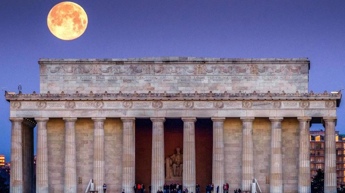 The full moon sets behind the Lincoln Memorial as people line the steps to watch the sun come up across the other end of the National Mall in Washington, Saturday, March 31, 2018.
