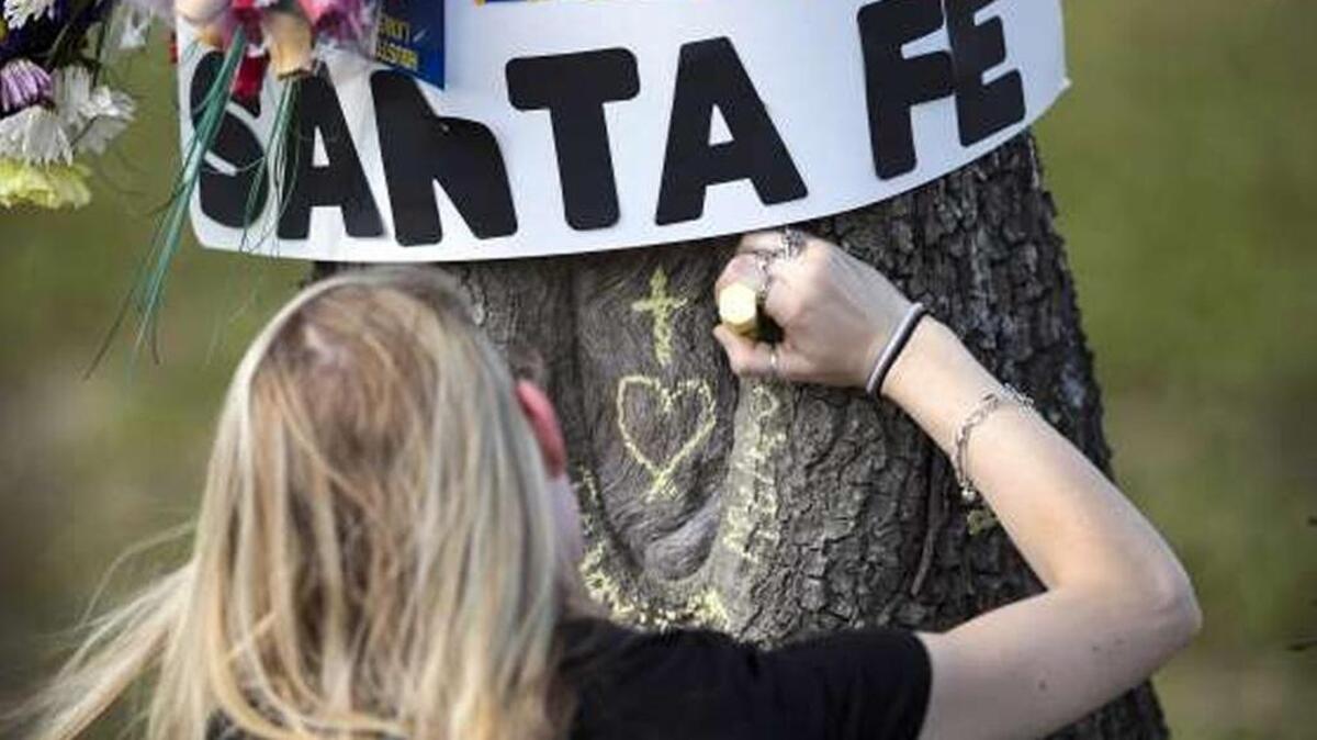 Danielle Shreve chalks a message onto a tree at a small memorial outside of Santa Fe High School following Friday’s shooting.