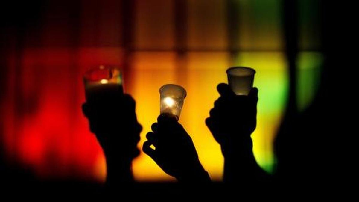 People raise candles against a rainbow-lit backdrop during a vigil for those killed in the mass shooting in Orlando.