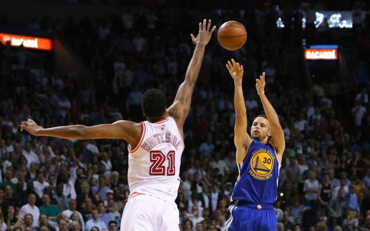 Golden State’s Stephen Curry hits a three pointer against Heat center Hassan Whiteside at AmericanAirlines Arena in Miami on February 24, 2016.