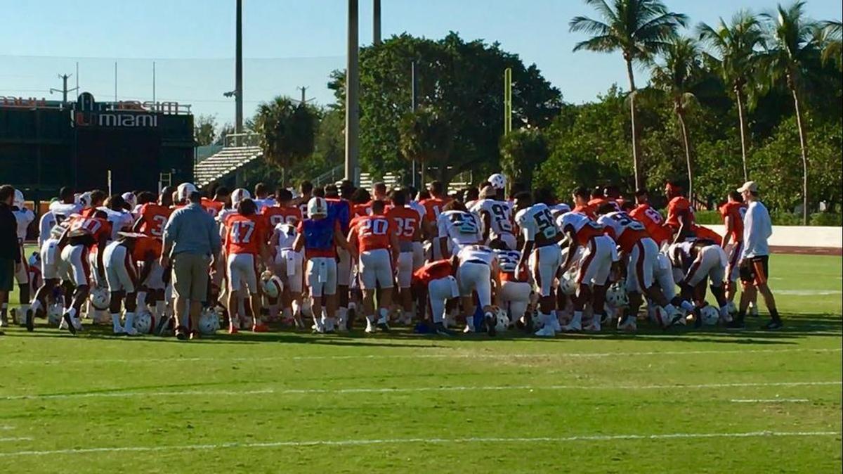 The Miami Hurricanes gather for a chat with coach Mark Richt after stretching during the first day of media availability as the Canes prepare for Wisconsin in the Capital One Orange Bowl.