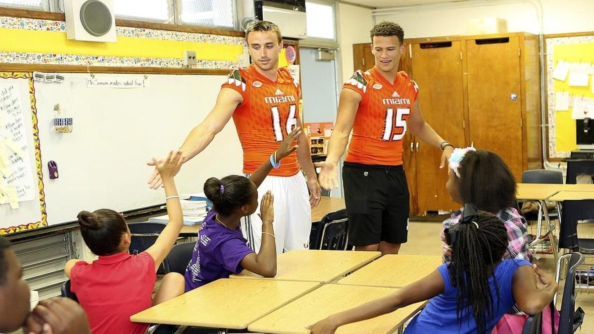 University of Miami Hurricanes punter Justin Vogel, left, and QB Brad Kaaya share high fives with fifth-graders at Frances S. Tucker Elementary School in Coconut Grove on Thurs., May 26, 2016. UM football players visited several classrooms and talked with students about the importance of a good education. Then they played football, basketball and kickball with students on a court and a field at the school, 3500 Douglas Rd. in Coconut Grove.