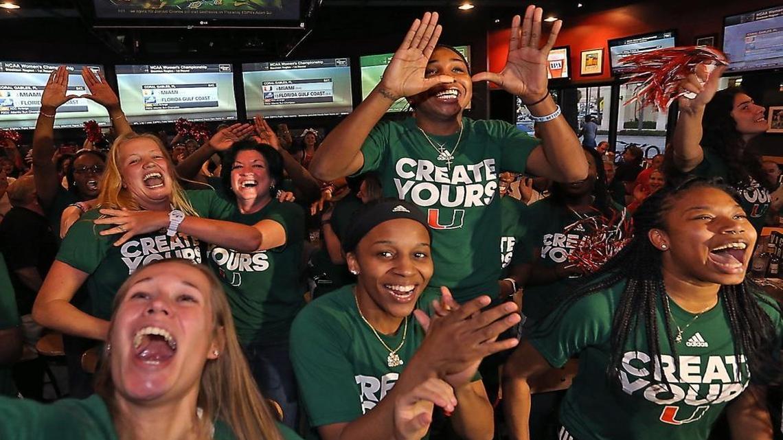 University of Miami head basketball coach Katie Meier (background) gets a hug from player Emese Hof as Jessica Thomas jumps up on a chair and throws up the U on Mon., March 13, 2017 as they realize they will be playing at home in the NCAA Tournament.