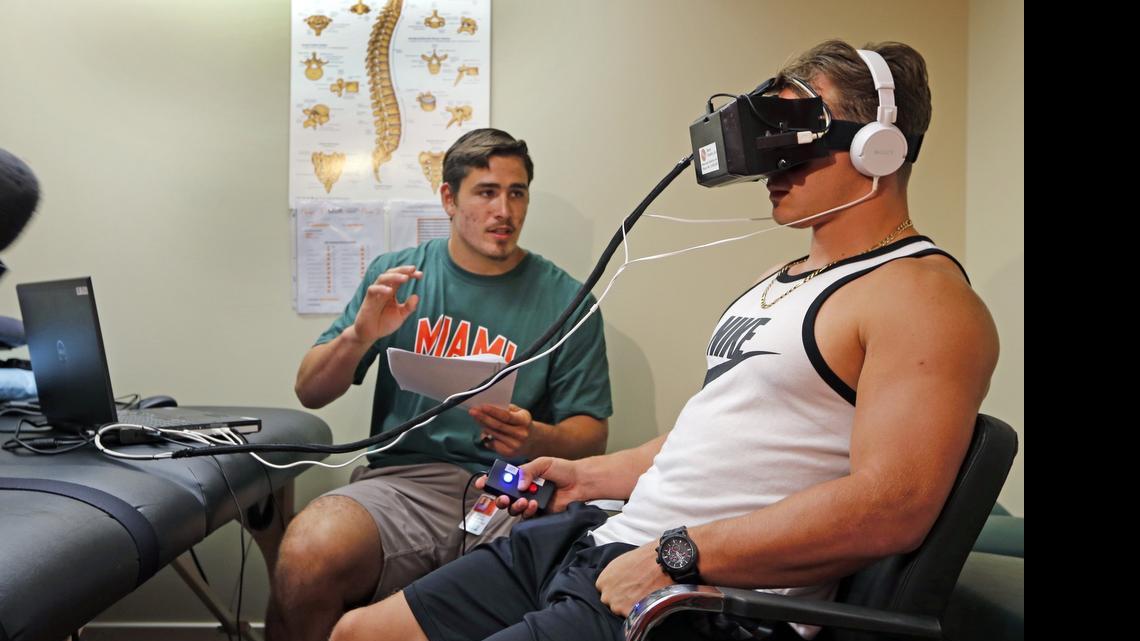 
University of Miami Sports Medicine research volunteer Tyler Waner gives football player Braxton Berrios instructions during testing with concussion goggles. 
