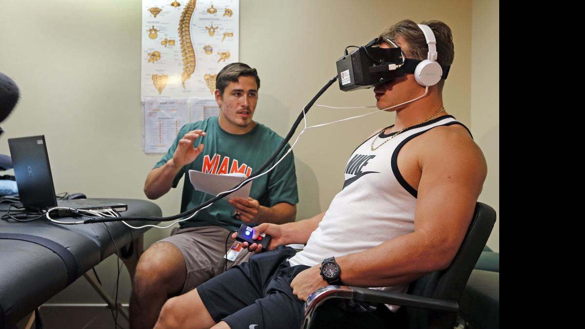 
University of Miami Sports Medicine research volunteer Tyler Waner gives football player Braxton Berrios instructions during testing with concussion goggles. 
