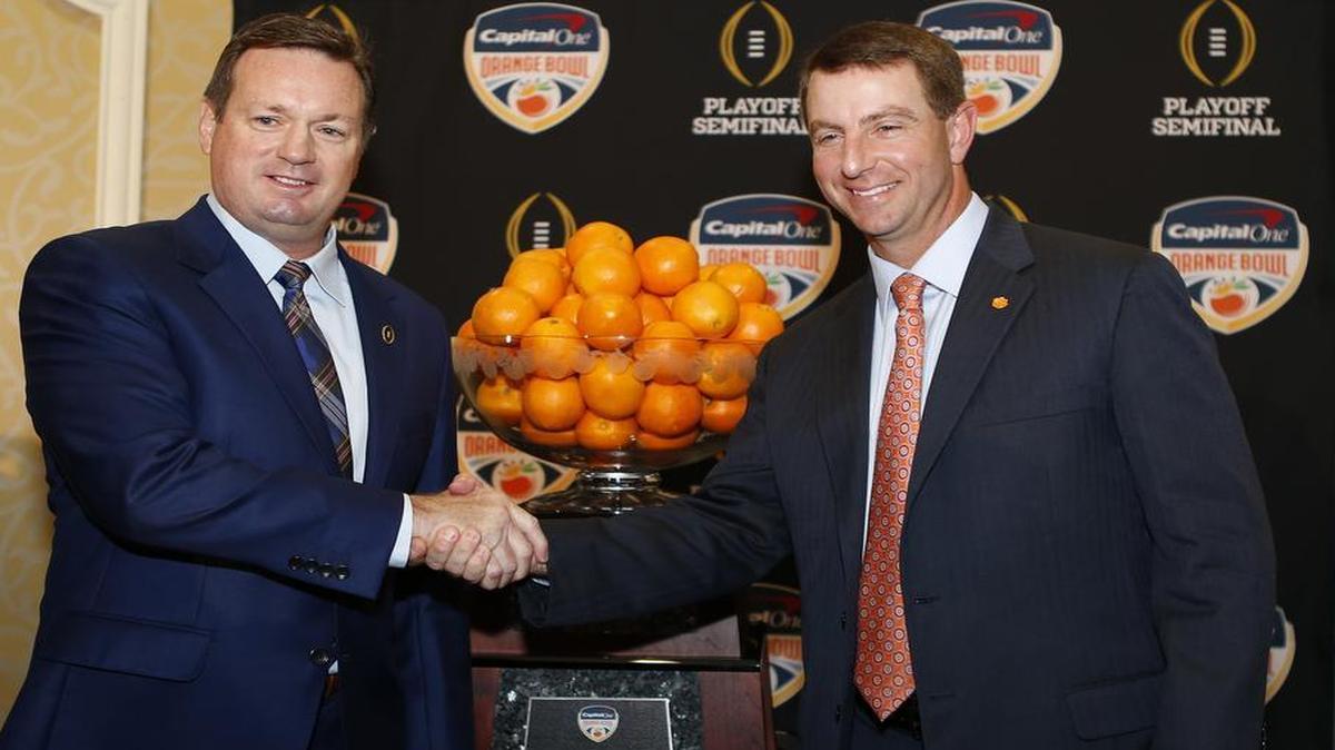 Oklahoma head coach Bob Stoops, left and Clemson head coach Dabo Swinney shake hands in front of the trophy during the coaches press conference Wednesday, Dec. 30, 2015, in Fort Lauderdale, Fla. Clemson is scheduled to play Oklahoma in the Orange Bowl NCAA college football game on New Year's Eve.