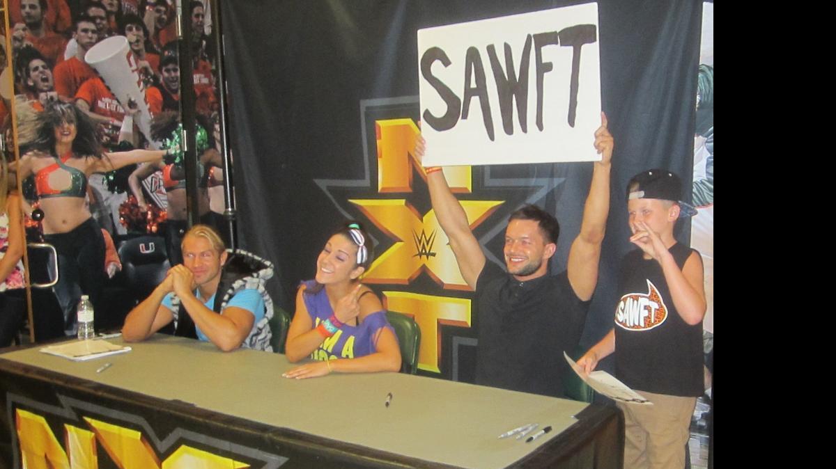 
NXT champ Finn Balor has some fun holding a sign made by a knowledgeable young fan (next to Balor) for the entertaining NXT tag team Enzo Amore and Big Cass Colin Cassady during a special NXT meet-n-greet before WWE NXT’s debut in Miami on Friday, July 24 at the Fieldhouse at the BankUnited Center at the University of Miami in Coral Gables. Also pictured are NXT standouts Tyler Breeze and Bayley.
