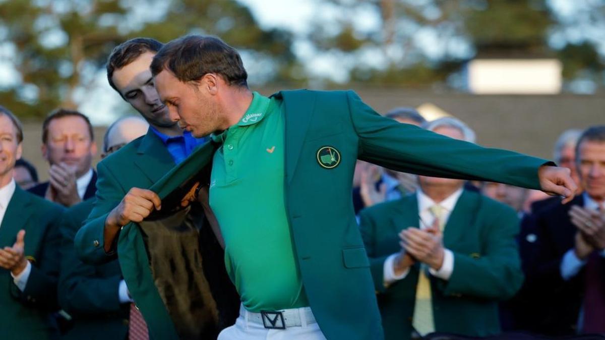 Defending champion Jordan Spieth, left, helps 2016 Masters champion Danny Willet, of England, put on his green jacket following the final round of the Masters golf tournament Sunday, April 10, 2016, in Augusta, Ga.