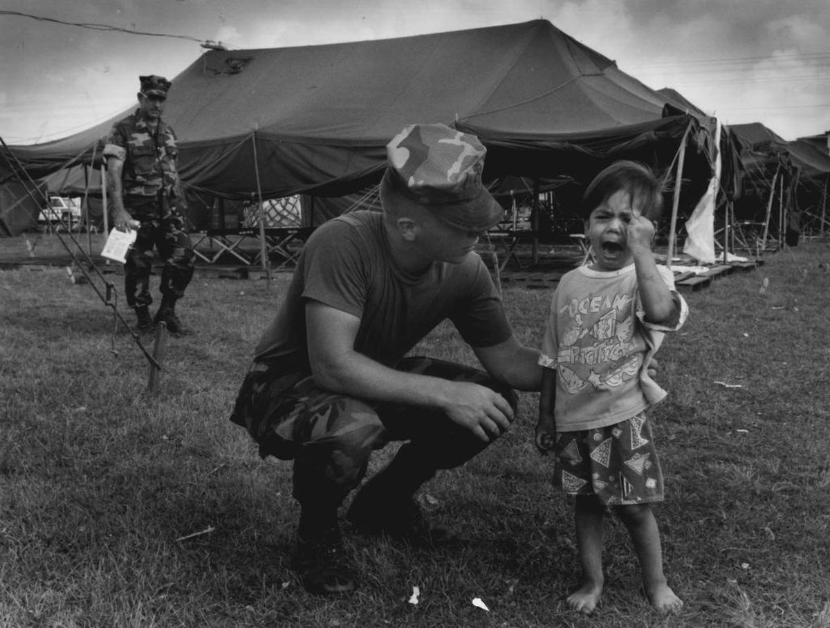 PFC Angelo Cruz Kneels down to comfort 2-year-old Cresencio Ruiz, as the boy moves into the tent city with his family in August 1992 shortly after Hurricane Andrew devastated Homestead. Cruz said, "I felt like he needed a hug."