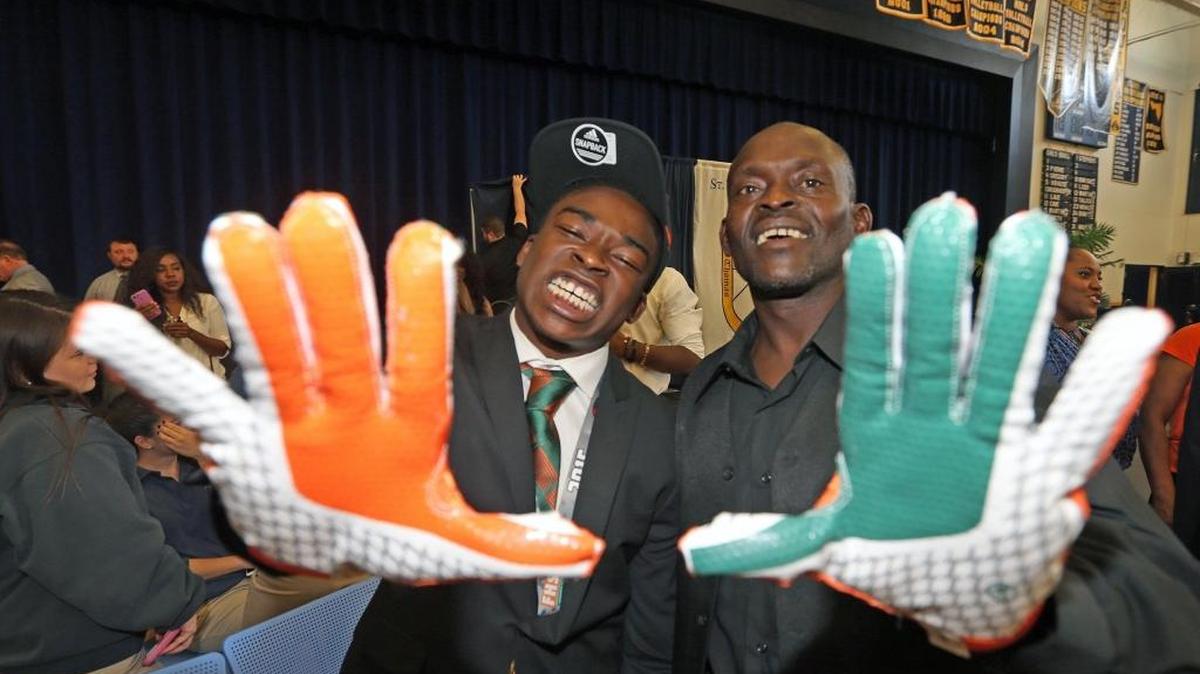 St. Thomas Aquinas receiver Sam Bruce displays the “U” gloves with father Sam Sr. after officially signing with the University of Miami on National Signing Day on Wednesday, Feb. 3, 2016 at St. Thomas Aquinas High in Fort Lauderdale.