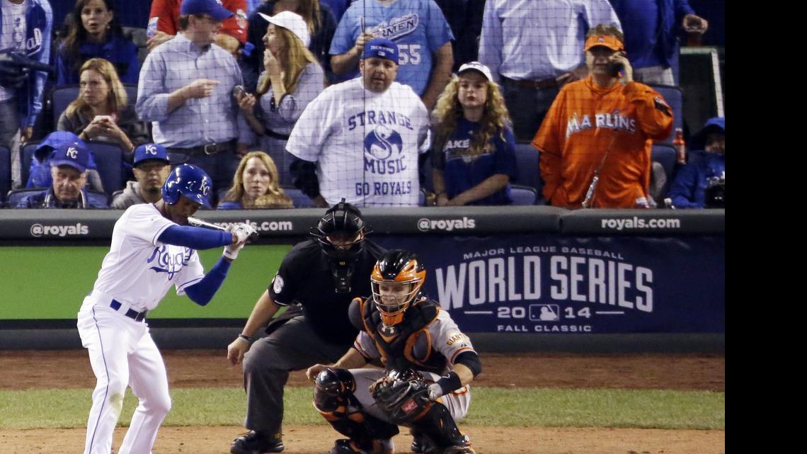 In this Wednesday, Oct. 22, 2014, photo, Miami Marlins fan Laurence Leavy, rear right, is shown wearing a bright orange Marlins jersey during Game 2 of baseball's World Series in Kansas City, Mo. Leavy's orange Marlins jersey made him easy to spot amid a sea of Kansas City Royals blue. He said a Royals official approached him offering to move him to the team owner's suite, but Leavy declined.

