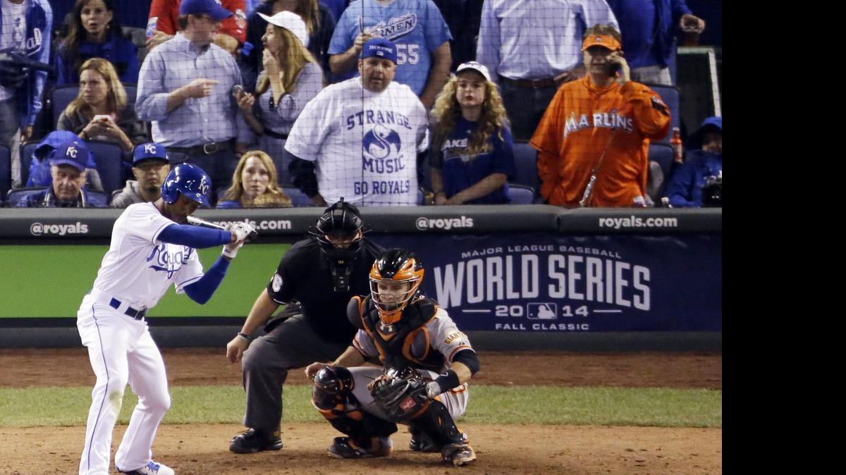 In this Wednesday, Oct. 22, 2014, photo, Miami Marlins fan Laurence Leavy, rear right, is shown wearing a bright orange Marlins jersey during Game 2 of baseball's World Series in Kansas City, Mo. Leavy's orange Marlins jersey made him easy to spot amid a sea of Kansas City Royals blue. He said a Royals official approached him offering to move him to the team owner's suite, but Leavy declined.
