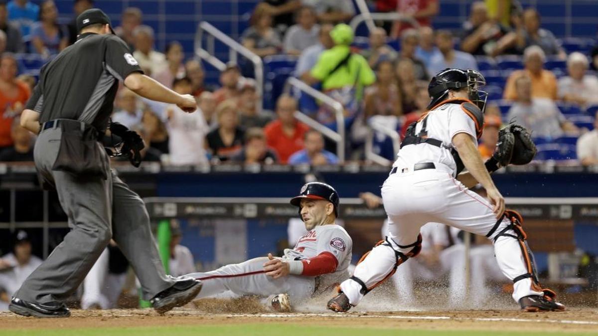 Washington Nationals' Danny Espinosa scores on an error by Miami Marlins center fielder Christian Yelich as catcher J.T. Realmuto awaits the throw, in the third inning of a baseball game, Wed., Sept. 21, 2016, in Miami. Home plate umpire Stu Scheurwater, left, watches the play.