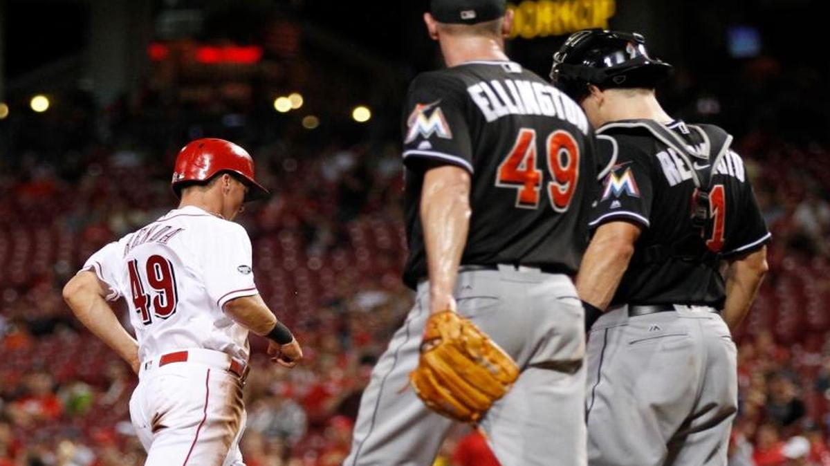 Cincinnati Reds' Tony Renda (49) scores on a sacrifice fly by Joey Votto as Miami Marlins relief pitcher Brian Ellington (49), and catcher J.T. Realmuto (11) watch during the seventh inning of a baseball game, Tues., Aug. 16, 2016, in Cincinnati.