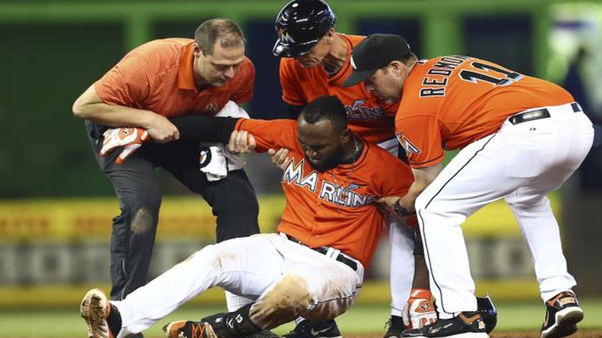 
Miami Marlins manager Mike Redmond (11) and third base coach Brett Butler, top center, along with a trainer help Marcell Ozuna to his feet after he hurt his leg during the seventh inning of a baseball game against the Washington Nationals in Miami, Sunday, Sept. 21, 2014. The Nationals won 2-1. 
