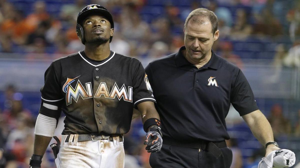 
Miami Marlins' Dee Gordon, left, walks off the field with head trainer Sean Cunningham, right, after sliding safely into first but dislocating his thumb in seventh inning of a baseball game against the Cincinnati Reds, Saturday, July 11, 2015, in Miami. The Marlins defeated the Reds 14-3. 
