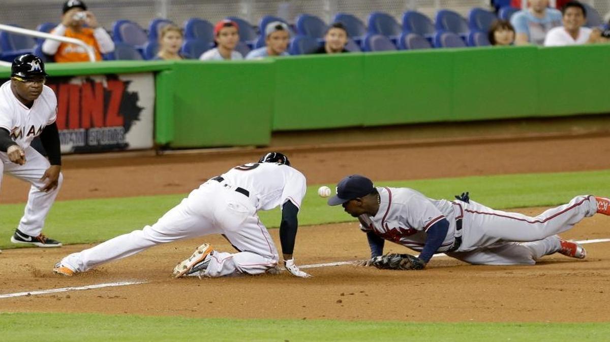 Miami Marlins' Dee Gordon (9) is safe at third base on a triple as Atlanta Braves third baseman Adonis Garcia, right, is unable to hold on to the ball as Marlins third base coach Lenny Harris, left, gives instructions, in the third inning of a baseball game, Thurs., Sept. 22, 2016, in Miami.