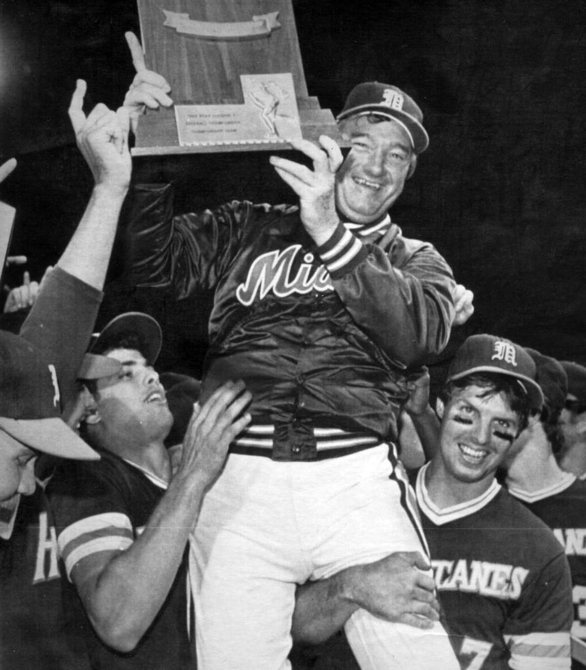 University of Miami baseball coach Ron Fraser holds the national championship trophy as team members Eddie Escribano (left) and Phil Lane (right) carry Fraser around the field following Miami's 9-3 win over Wichita Sate in the 1982 NCAA College World Series.