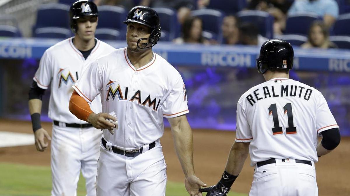 Miami Marlins' Giancarlo Stanton, center, is congratulated by teammate J.T. Realmuto (11) after Stanton and Christian Yelich, left, scored on a single by Marcell Ozuna (13) against the Washington Nationals during the first inning of a baseball game, Mon., April 18, 2016, in Miami.