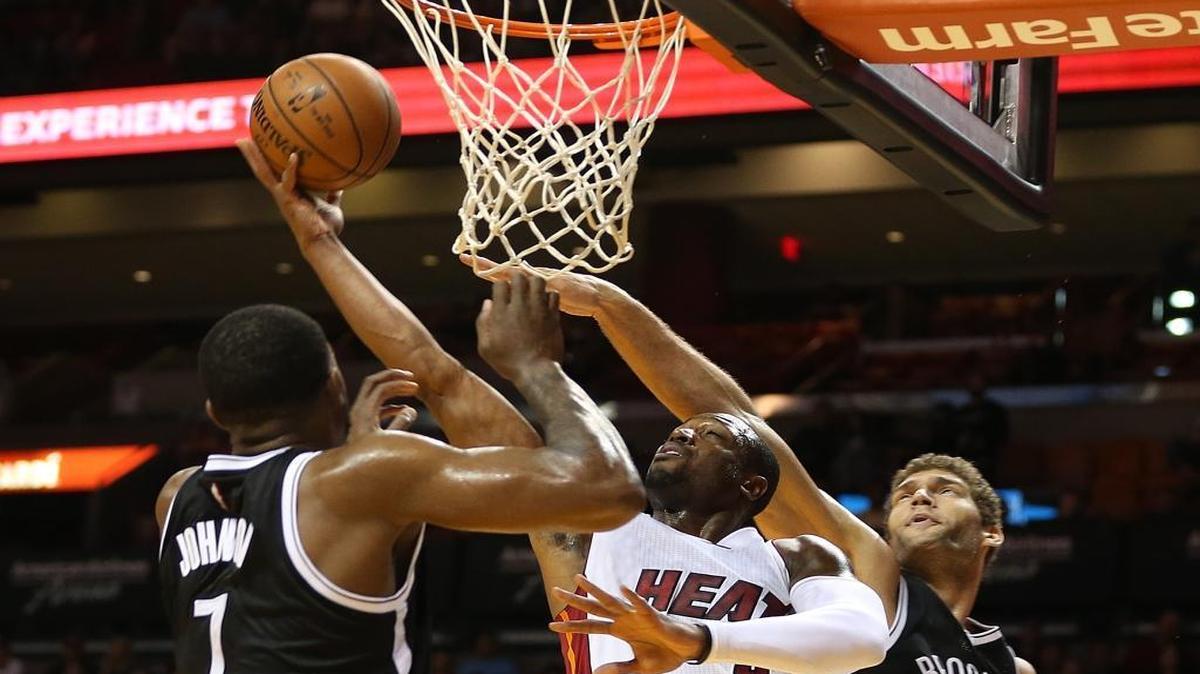 Dwyane Wade, of the Miami Heat, goes to the basket against Joe John and Brook Lopez, of the Brooklyn Nets, in the first quarter of a game at AmericanAirlines Arena in Miami on Monday, December 28, 2015.