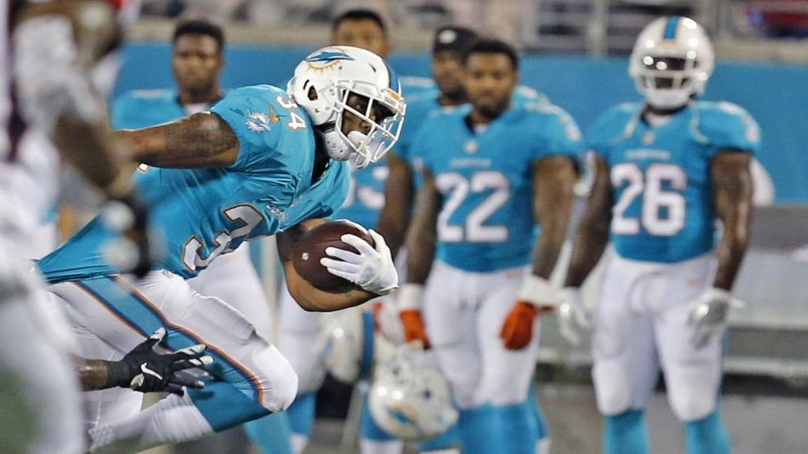 Dolphins Arian Foster, 34, breaks a tackle in the first quarter as Isaiah Pead, 22, Damien Williams, 26, watch on the sideline at Camping World Stadium in Orlando, Florida, Aug. 25, 2016. The trio are among the five running backs coach Adam Gase kept Saturday.