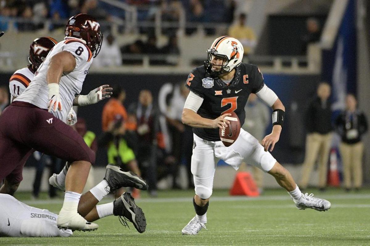 Oklahoma State quarterback Mason Rudolph (2) scrambles in front of Virginia Tech defensive end Houshun Gaines (11) and defensive tackle Ricky Walker (8) during the second half of the Camping World Bowl NCAA college football game Thurs., Dec. 28, 2017, in Orlando, Fla. Oklahoma State won 30-21.